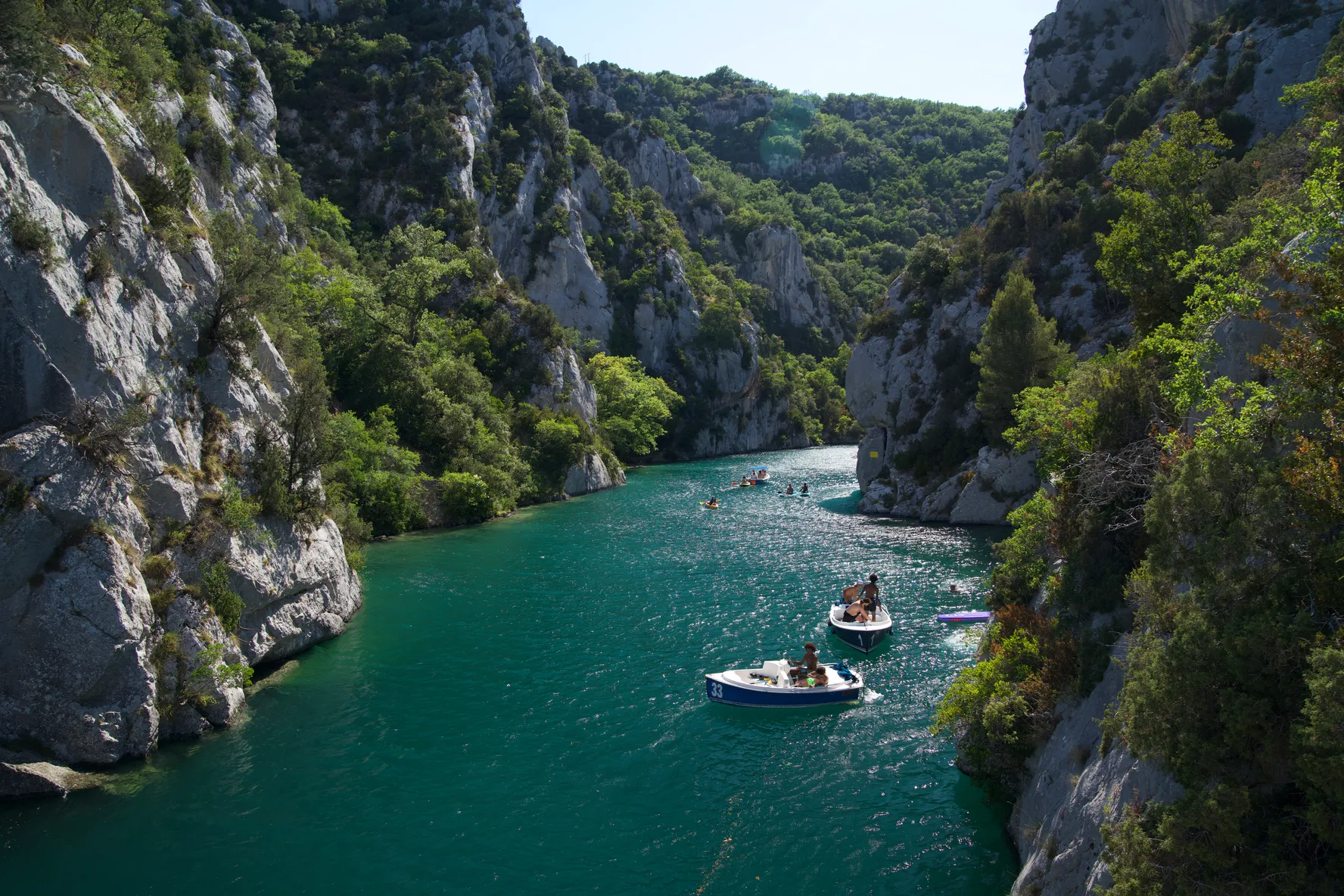 Small boats on the turquoise water of the lower Verdon gorge, between limestone cliffs