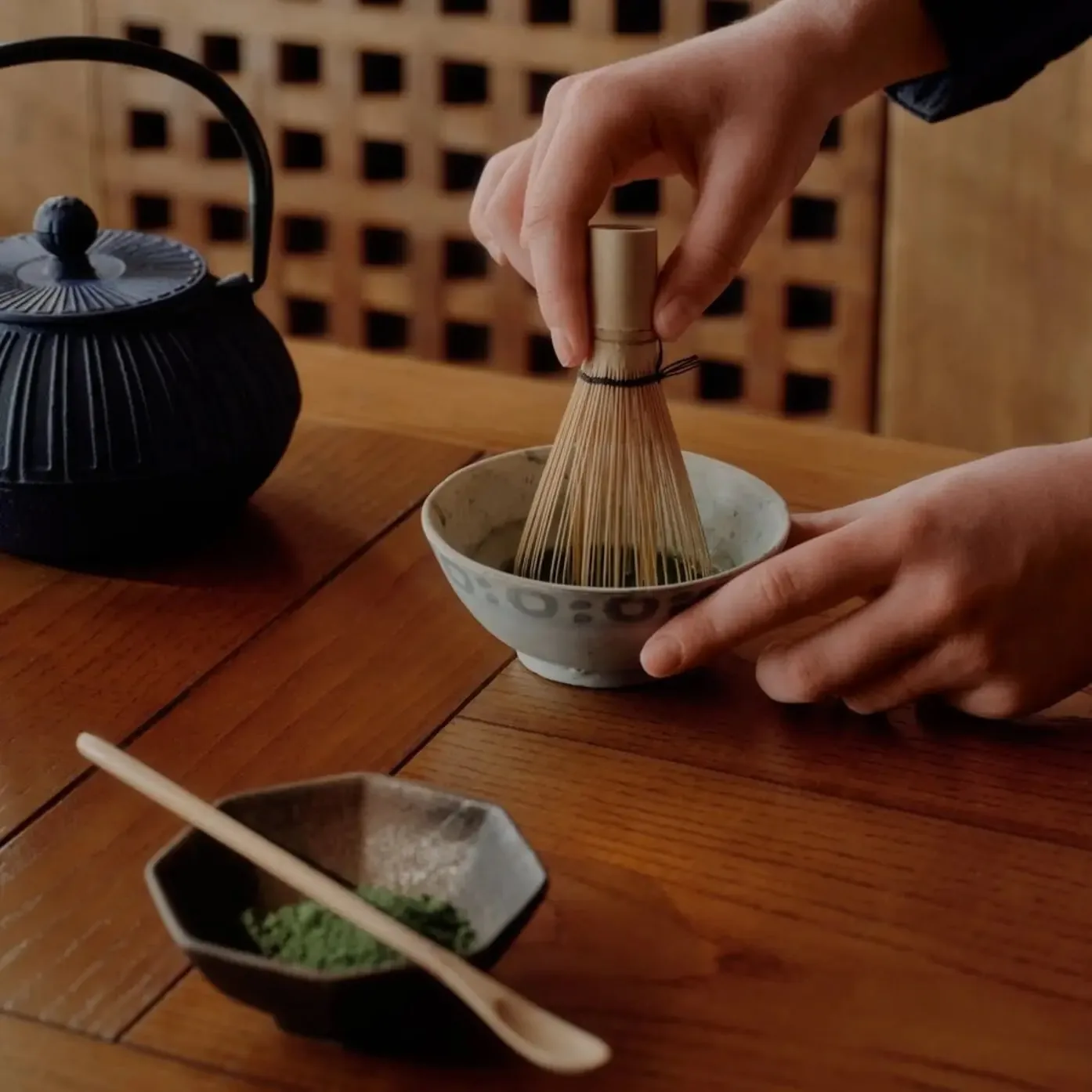 Japanese tea ceremony with a bamboo whisk stirring matcha beside a cast iron teapot