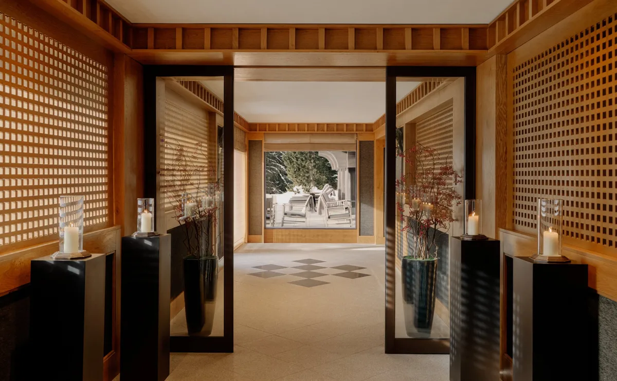 Entry corridor with mirrored screens, candlelit pedestals, and a checkerboard floor leading outside