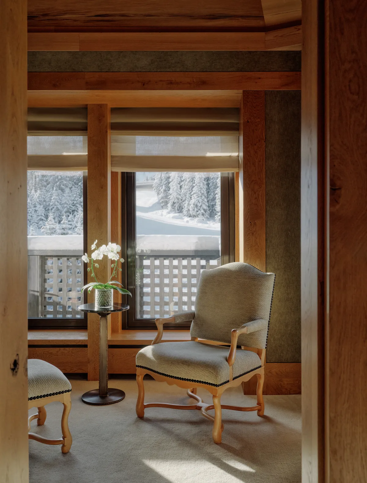 Reading nook with an upholstered armchair, ottoman, and orchid table beside a snowy window