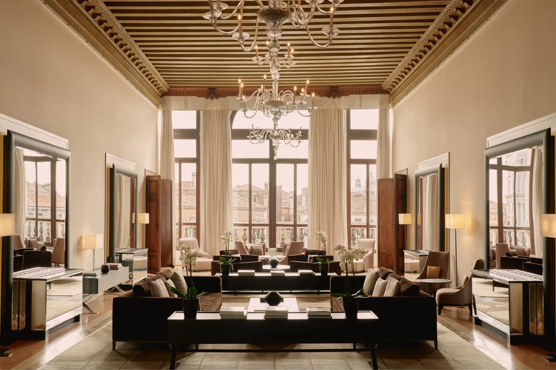 A luminous salon with a barrel-vaulted ceiling, tall arched windows, black upholstered seating, and marble flooring