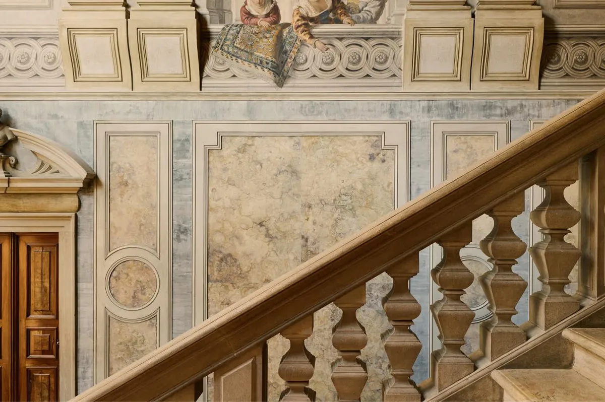 A marble staircase with ornamental railings, painted ceiling with classical medallions, and cream walls