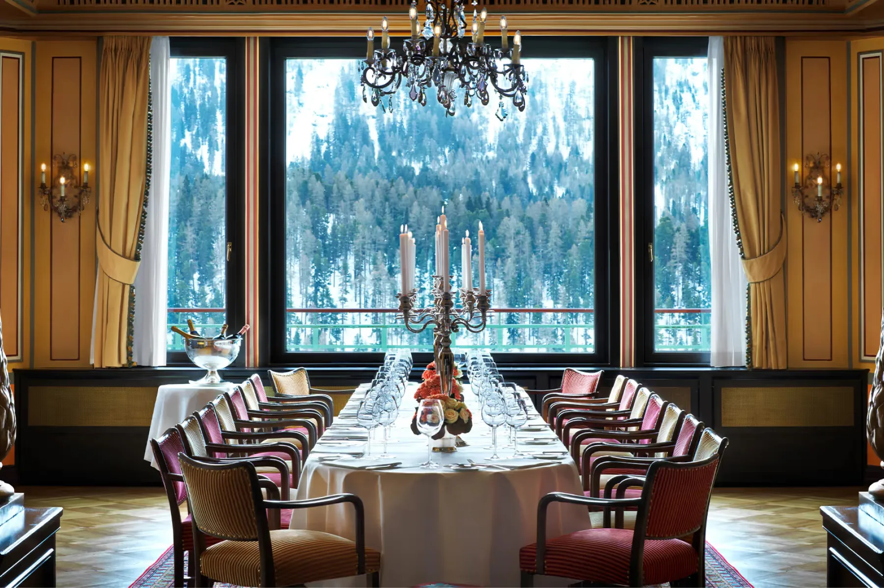 Long dining table with burgundy chairs, wood paneling, and alpine mountain views