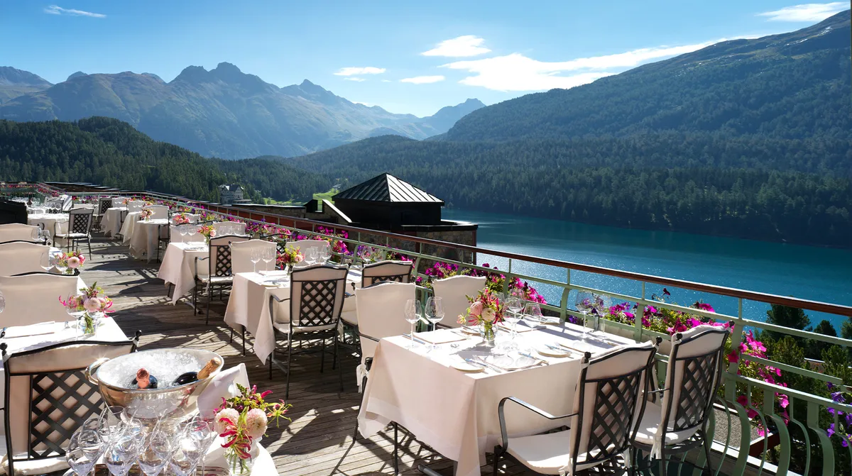 Outdoor terrace with white tablecloths overlooking blue lake and snow-capped peaks