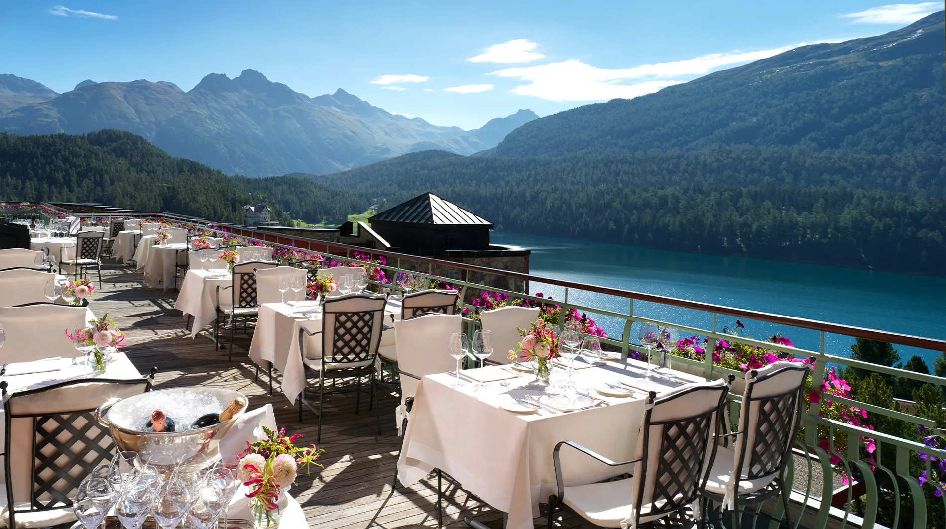 Outdoor terrace with white tablecloths overlooking blue lake and snow-capped peaks