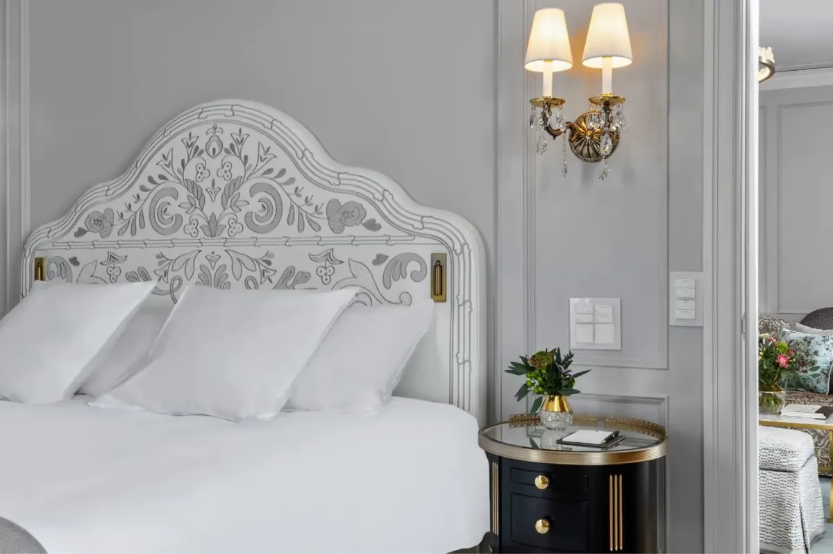 Bedroom with ornate white headboard, gold sconces, and bedside nightstands