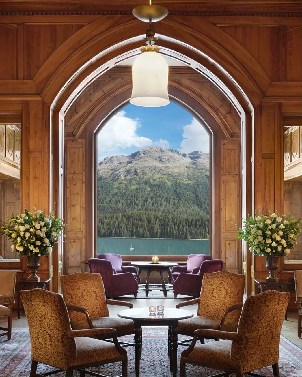 Wood-paneled library with ornate archway framing alpine lake and mountain vista