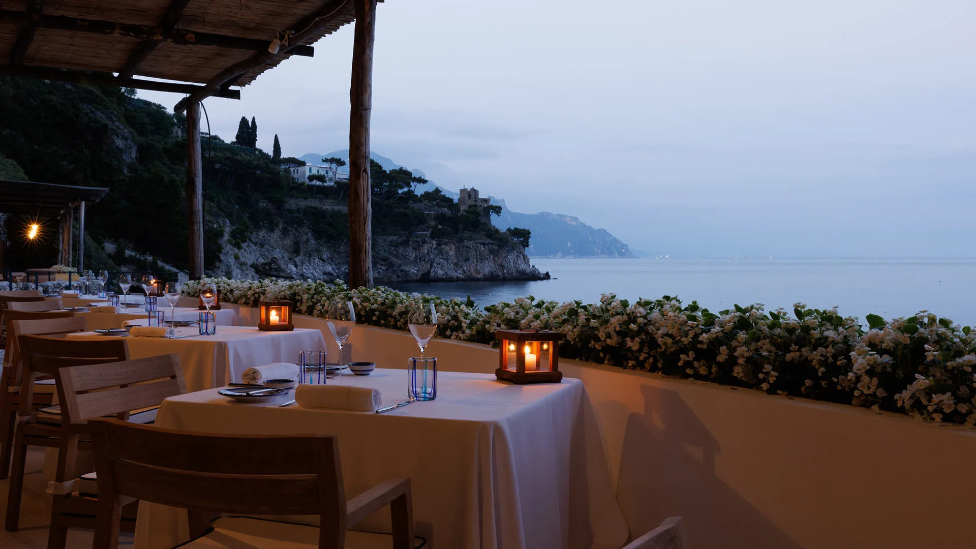 Candlelit dining setup on clifftop terrace at dusk with mountain horizon