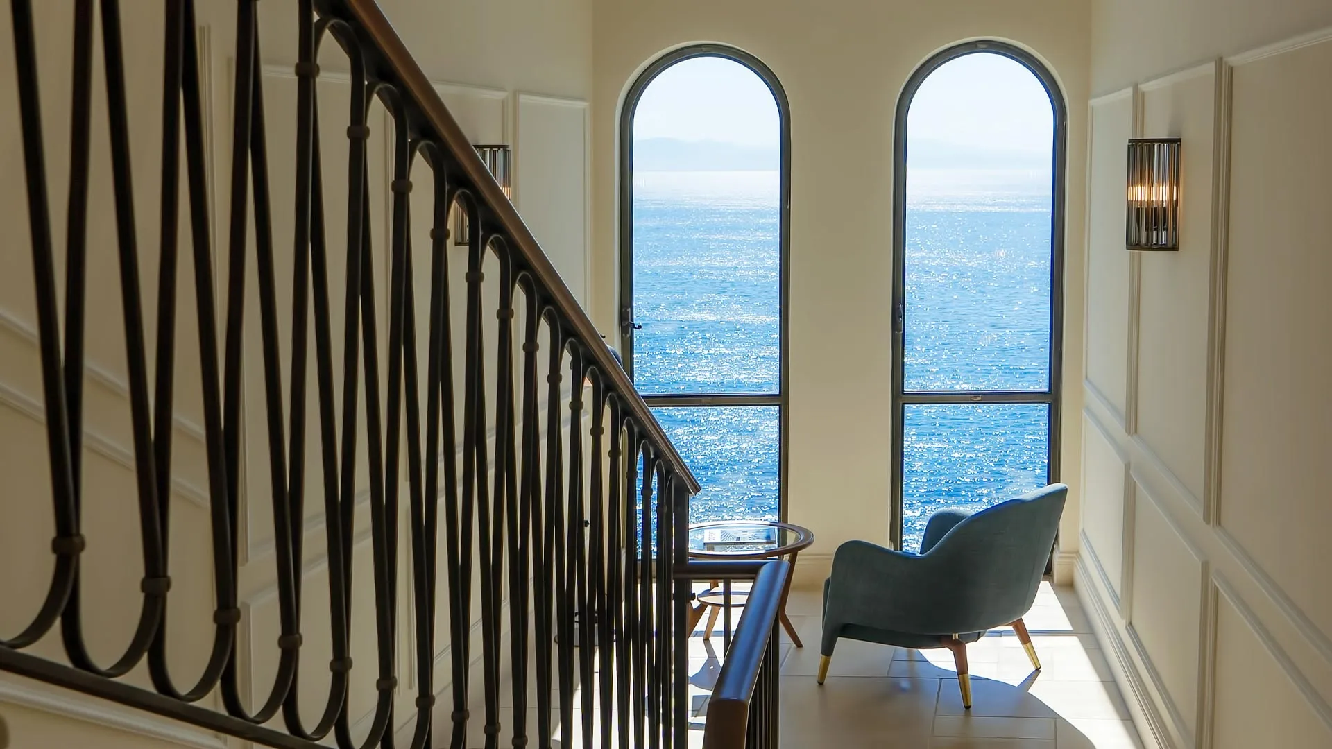 Stairwell with black railings framing arched windows overlooking the sea