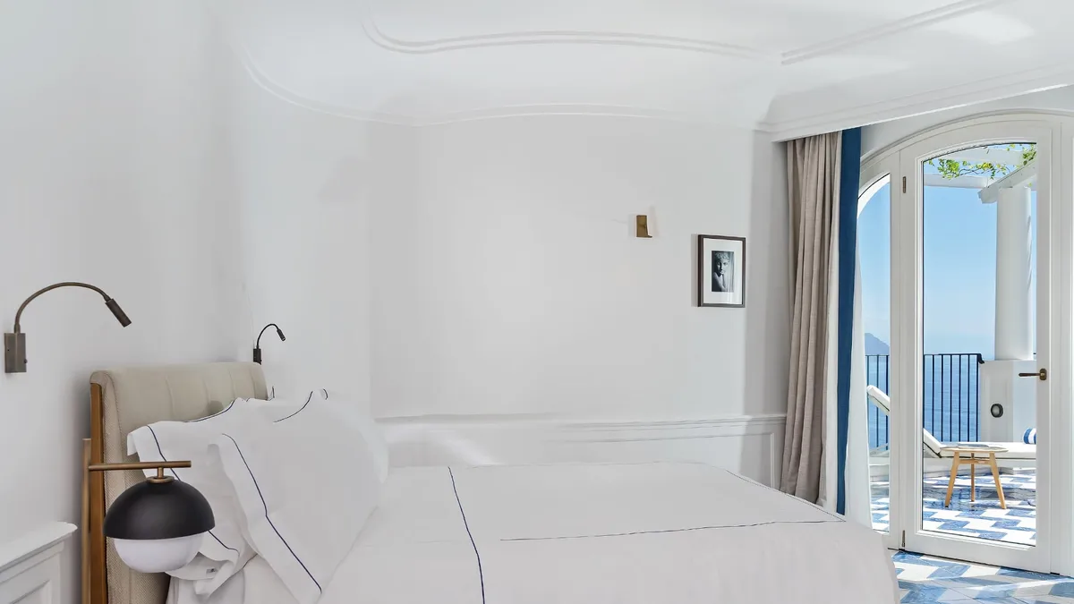 Minimalist bedroom with white bedding and ocean vista through glass doors at dusk