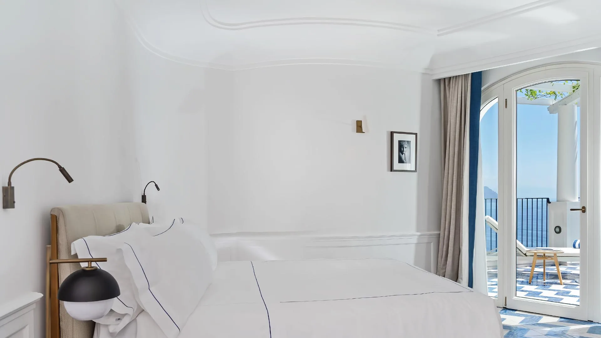 Minimalist bedroom with white bedding and ocean vista through glass doors at dusk