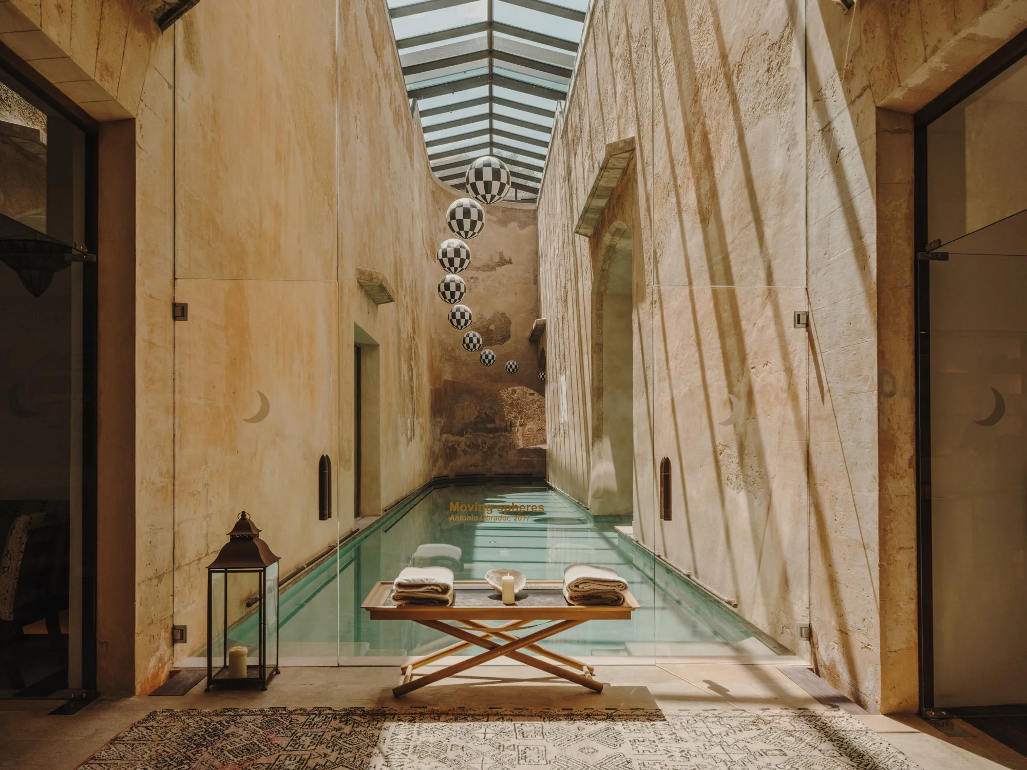A spa corridor with turquoise pool, smooth stone walls, wooden columns, and glass skylight