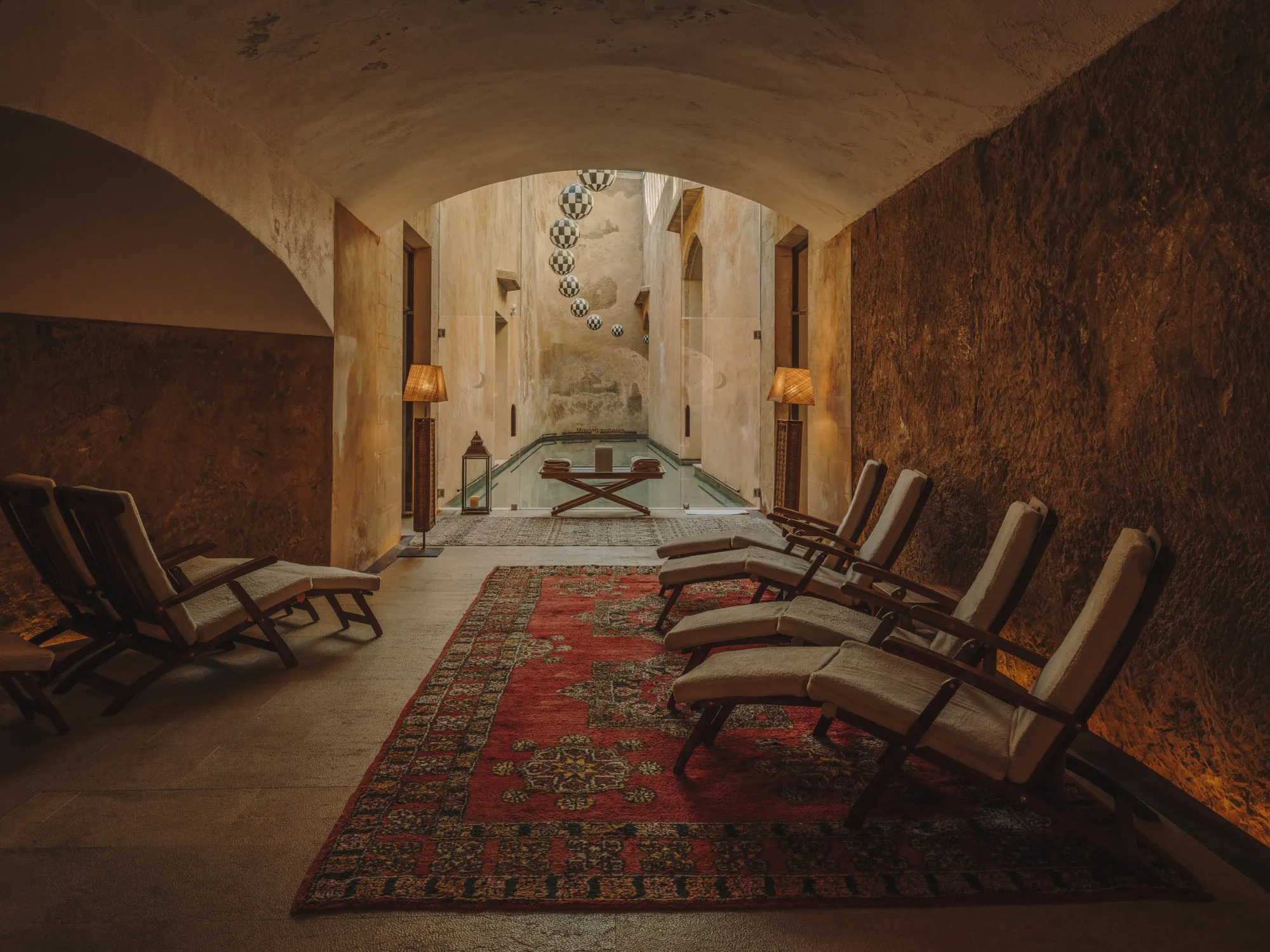 A stone hammam interior with arched ceilings, olive-toned walls, and centered relaxation spaces