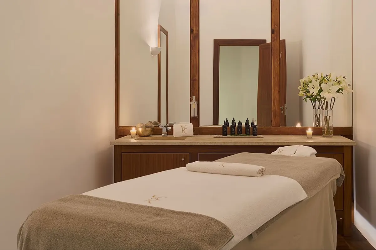 A massage room with a treatment table, mirror, white orchids, and warm natural light