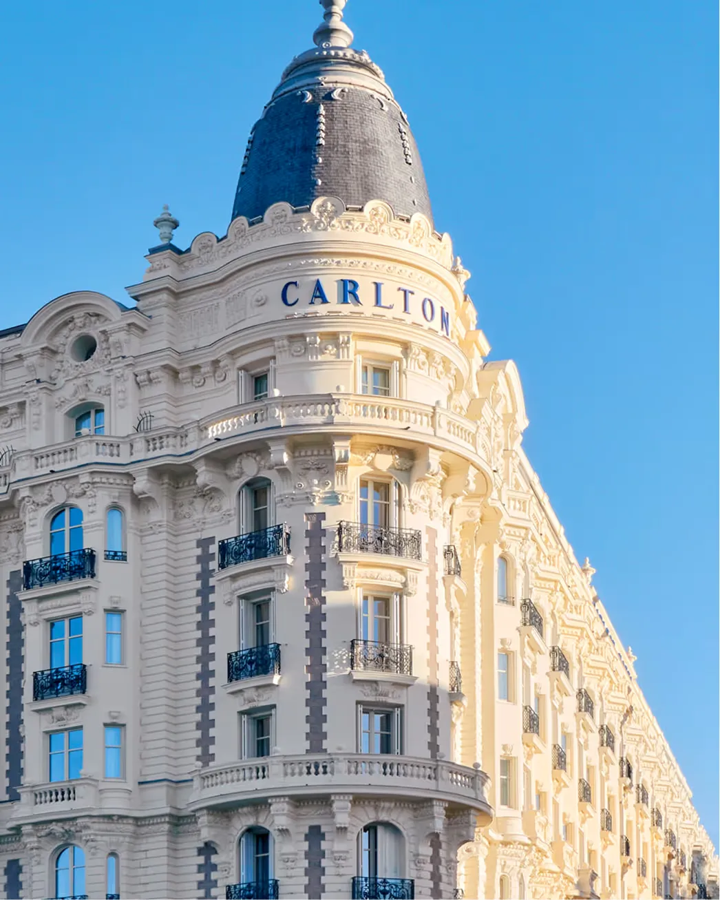 Full view of Carlton Cannes building showing the distinctive domed turret and multi-story limestone exterior with blue-framed windows