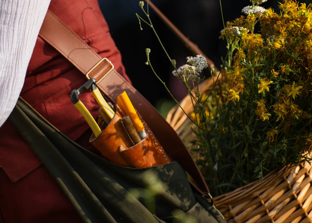 A close up of leather tool pouches and pruning shears against wildflowers and a canvas apron