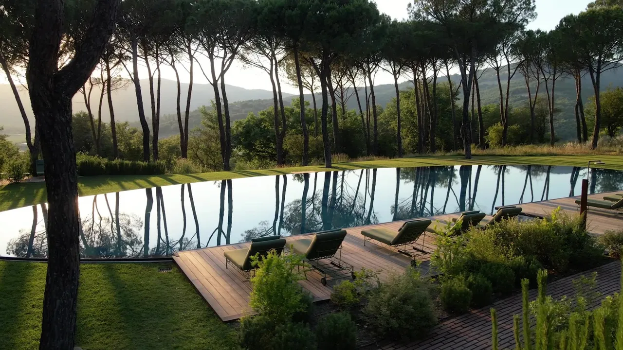 A reflecting pool framed by umbrella pines and a wooden sun deck, hills glowing gold beyond the trees