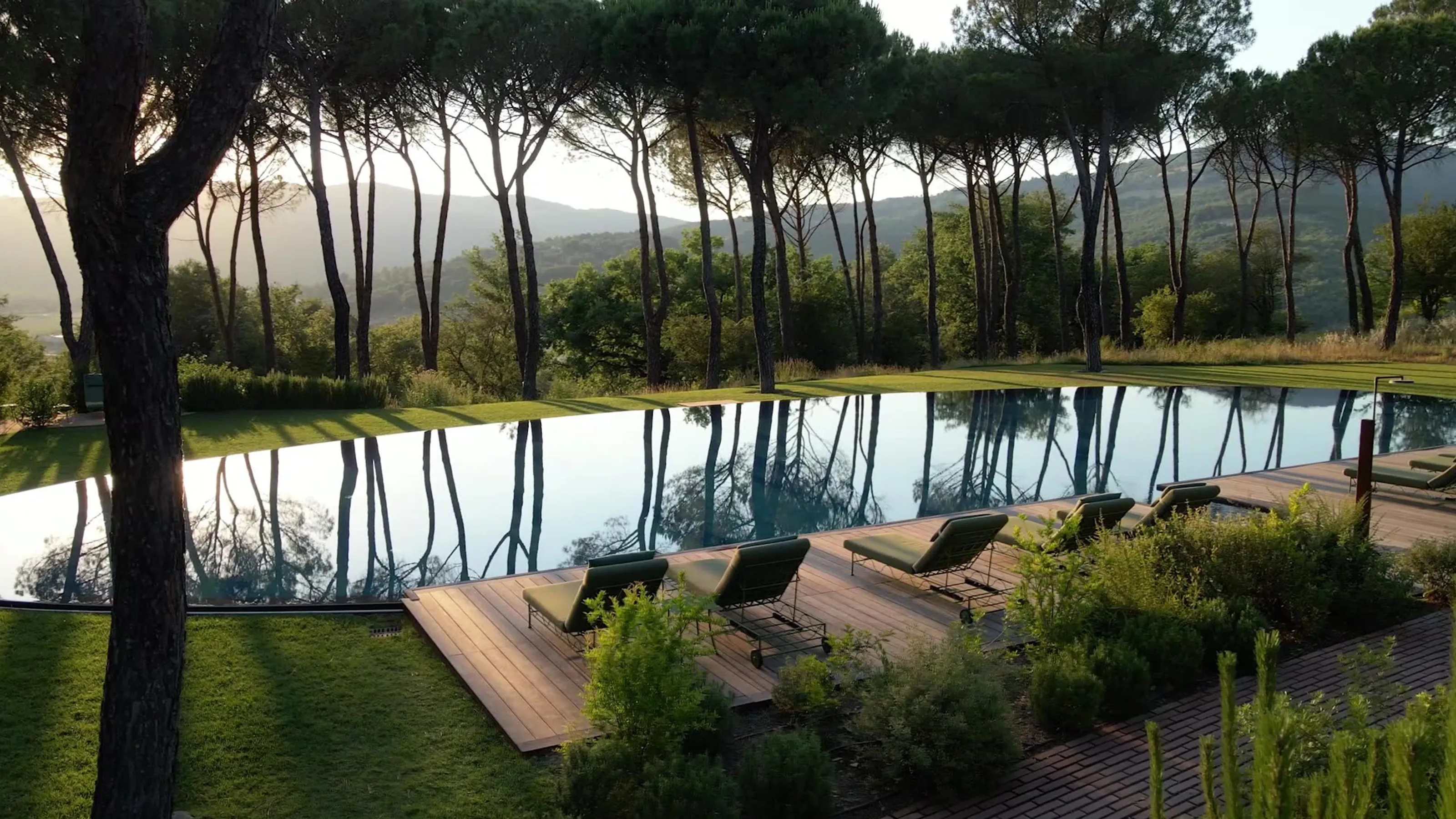 A reflecting pool framed by umbrella pines and a wooden sun deck, hills glowing gold beyond the trees