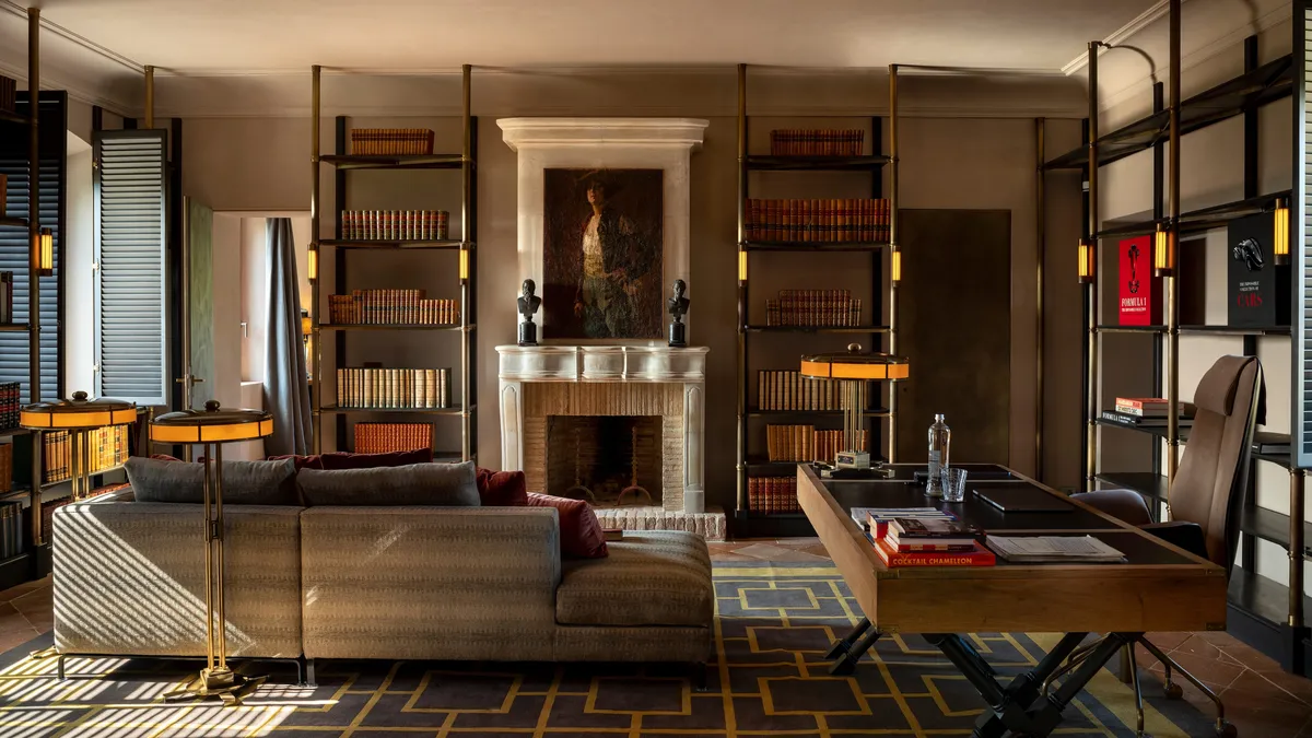 A library lounge with a stone fireplace, ladder shelving, and leather sofas around a brass legged table