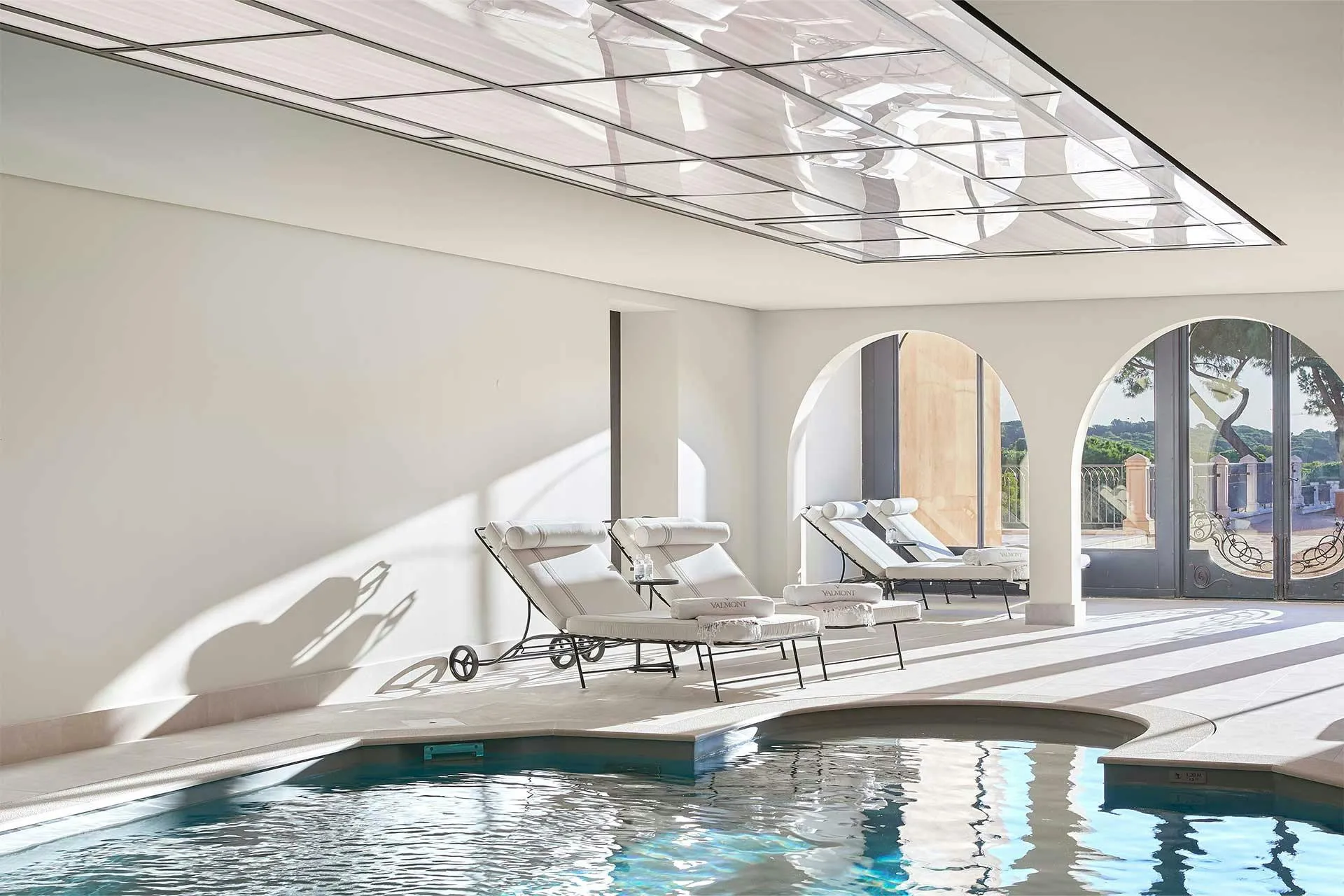 Indoor pool with skylights, white loungers, and bright natural illumination
