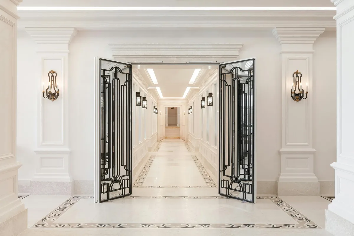 Interior hallway with white stone walls, ornate brass sconces, and decorative iron double doors