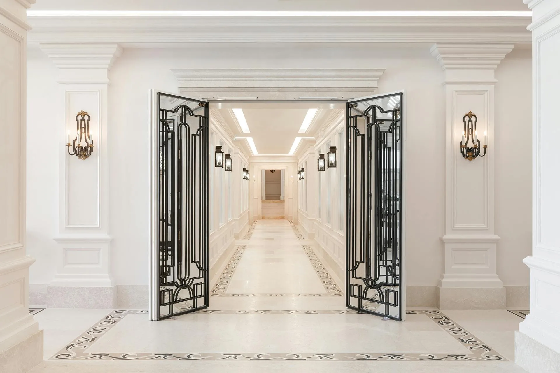 Interior hallway with white stone walls, ornate brass sconces, and decorative iron double doors