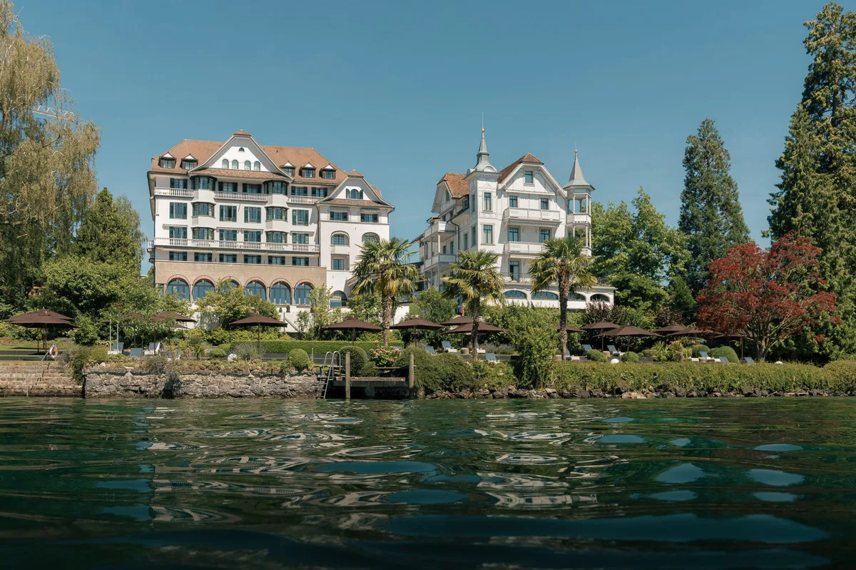 Hotel building complex seen from Lake Lucerne waterside, green grounds and manicured landscaping