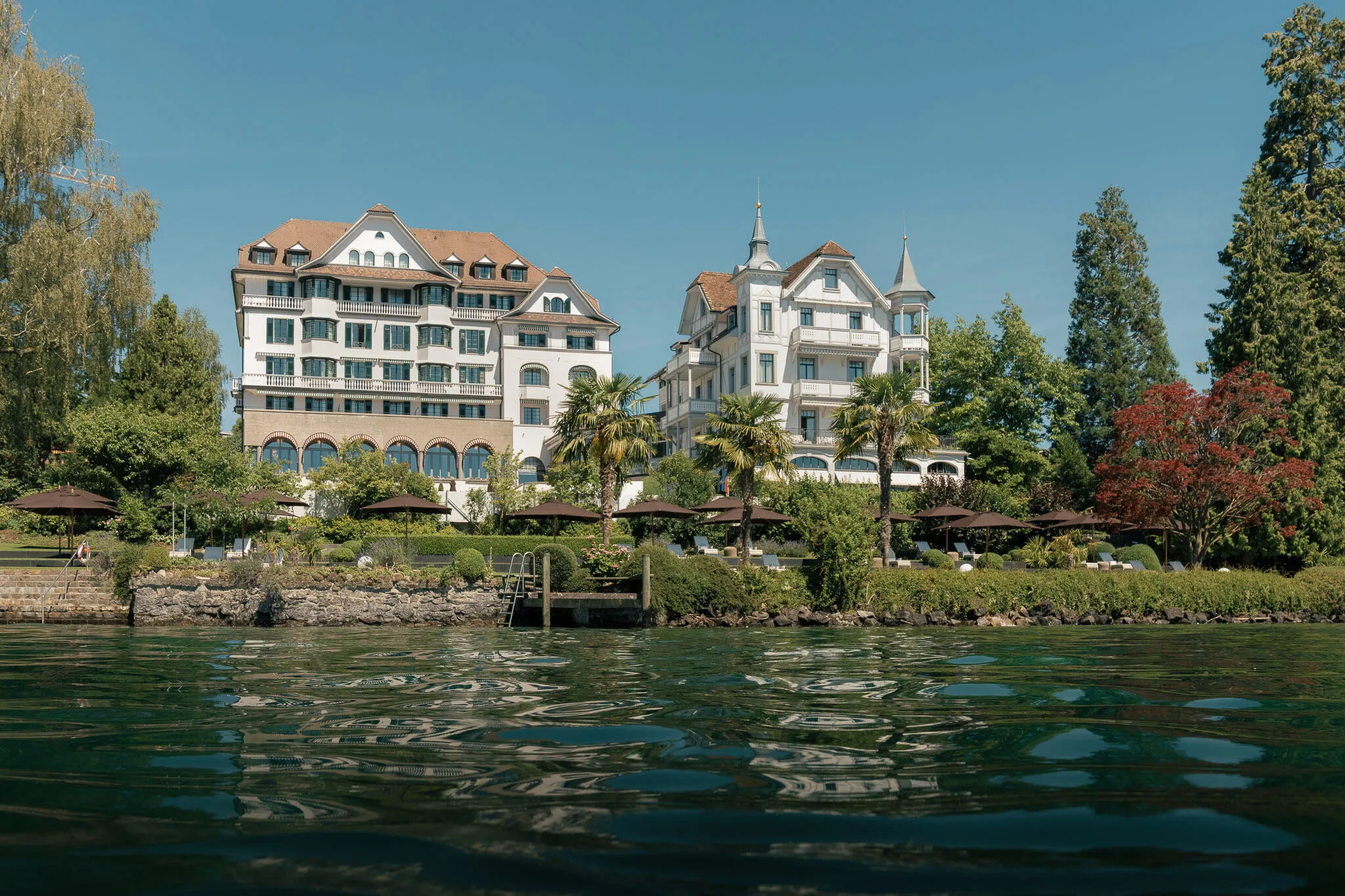 Hotel building complex seen from Lake Lucerne waterside, green grounds and manicured landscaping
