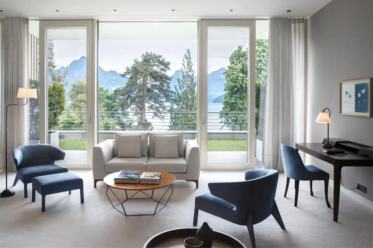 Modern sitting area with large windows, gray sofa, wood accent table, and Alpine views