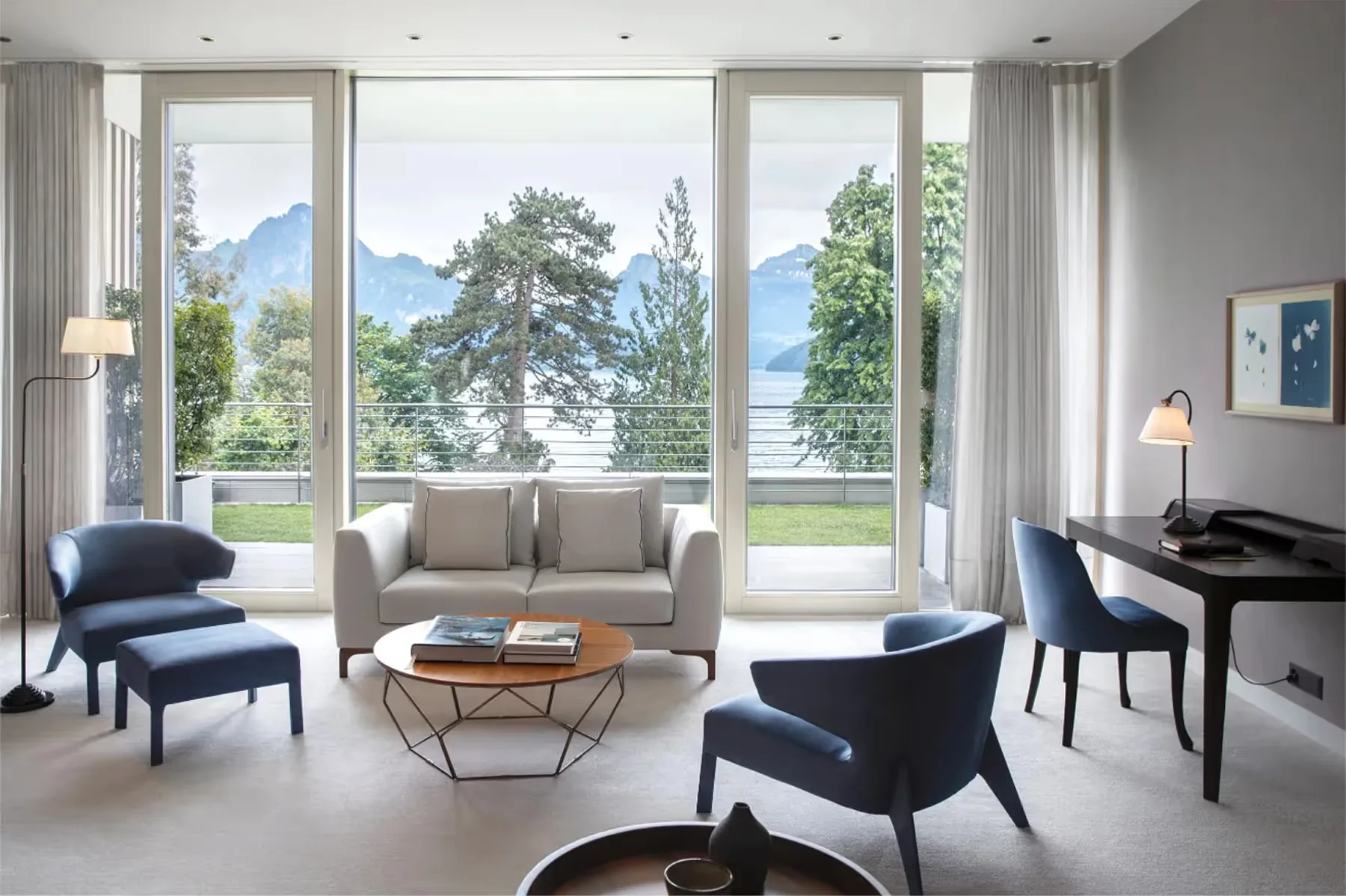 Modern sitting area with large windows, gray sofa, wood accent table, and Alpine views
