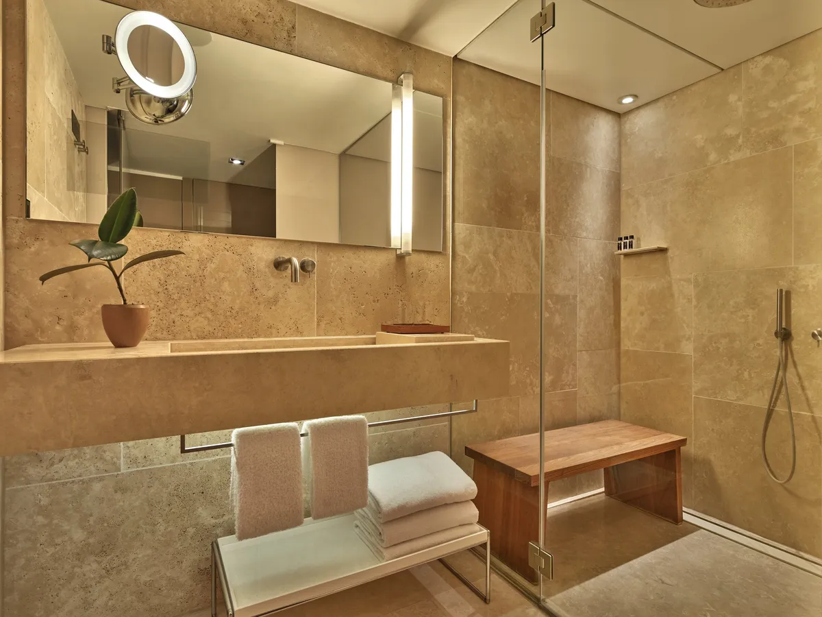 Spa-inspired bathroom with travertine walls, large mirror, and towel warming racks