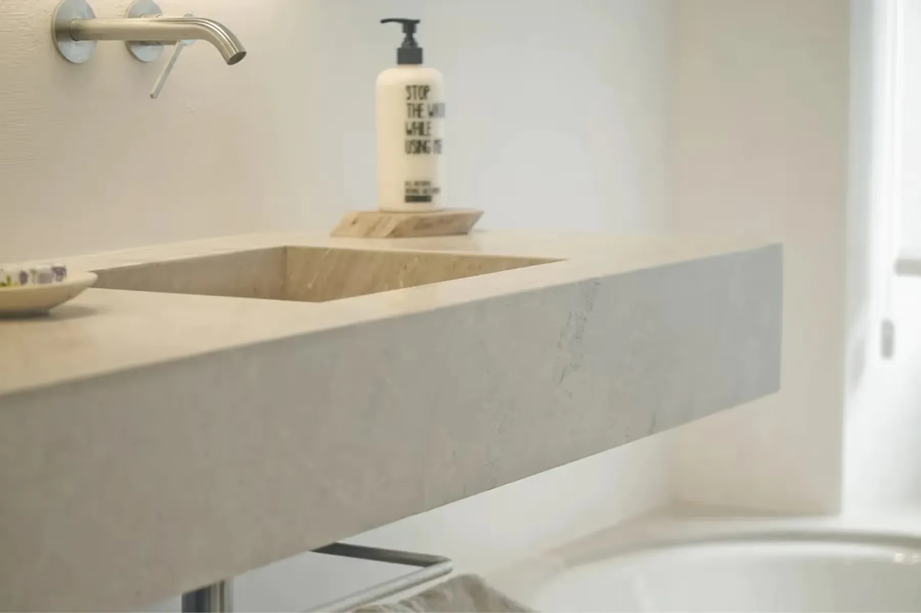 Minimalist concrete vanity with integrated sink, brass fixtures, and natural side lighting