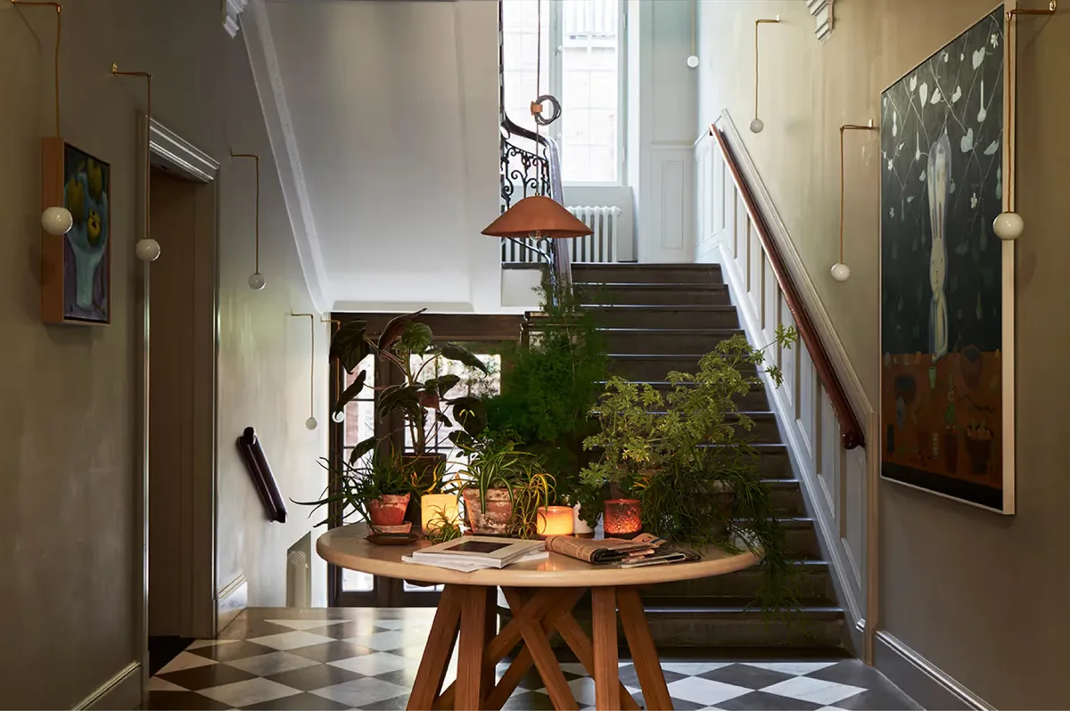 A cream hallway with potted plants on a round wooden table beneath a staircase