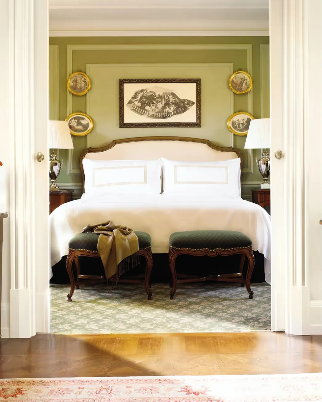 View through open doorways into a bedroom with pale green headboard and white bedding