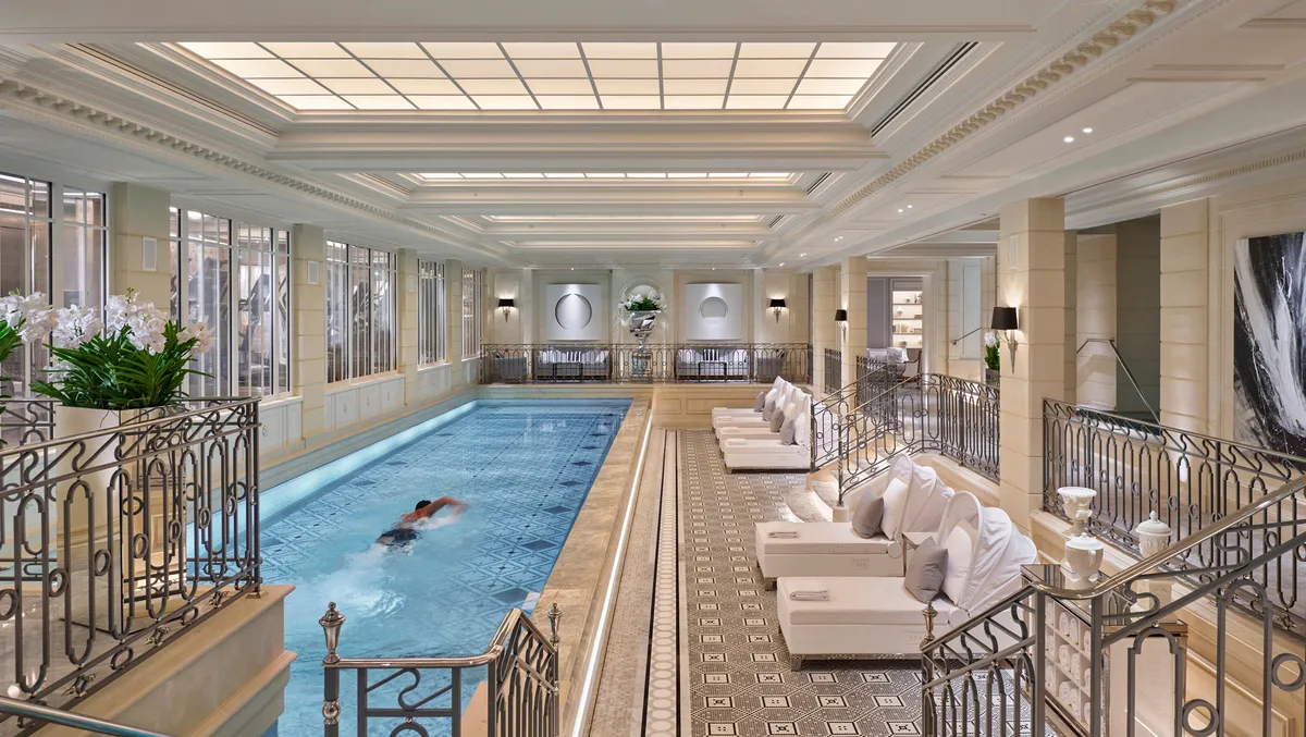 An indoor swimming pool surrounded by beige loungers and glass railings