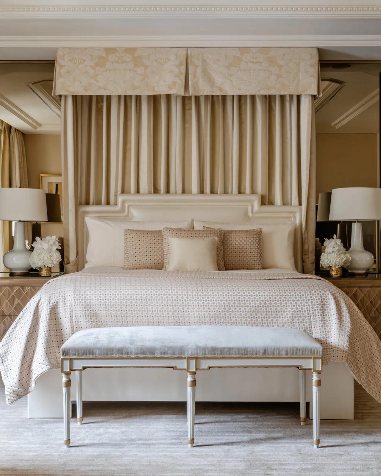 A bedroom with cream furnishings, coordinated drapes, and a bench at the foot of the bed