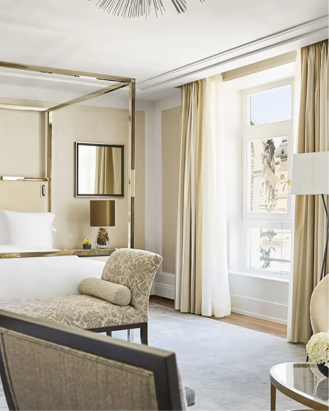 A suite bedroom with canopy bed, gold accents, and French doors opening to a balcony overlooking the city