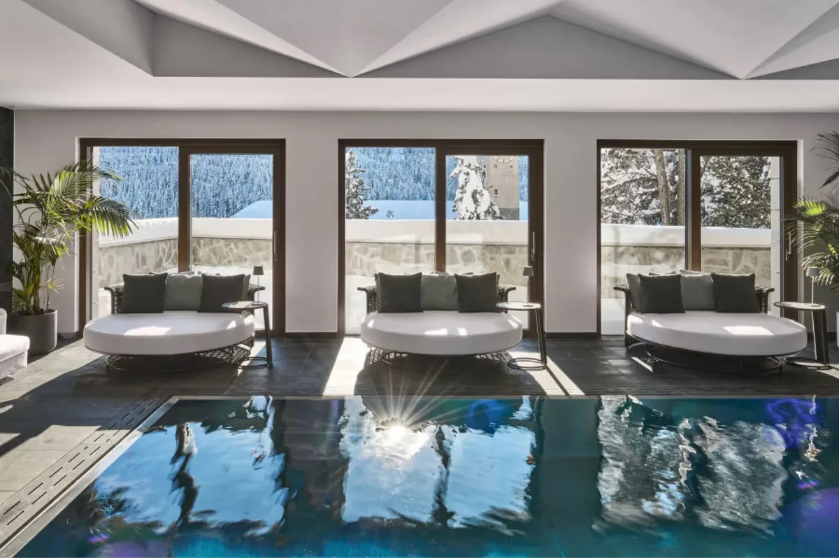 Indoor pool with blue water, large windows, loungers, and alpine landscape beyond