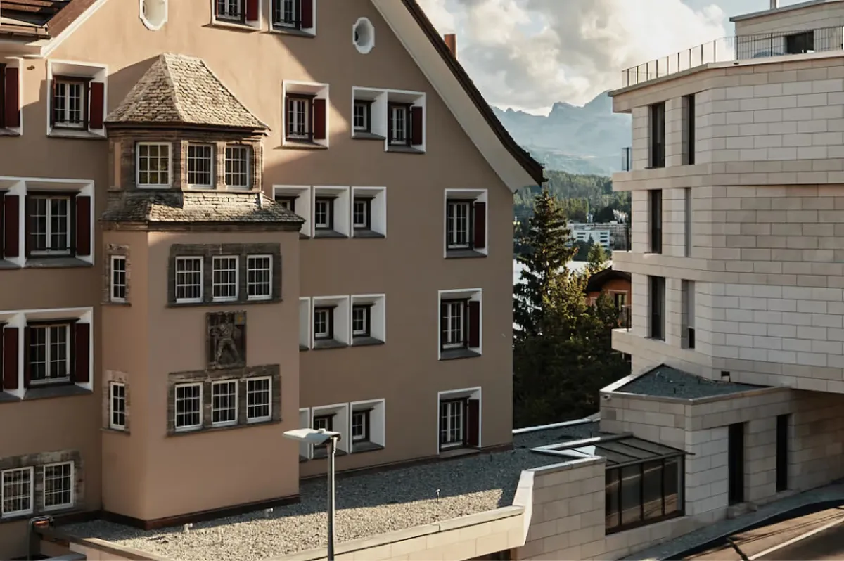 Historic stone buildings with mountains in the distance and alpine meadow below