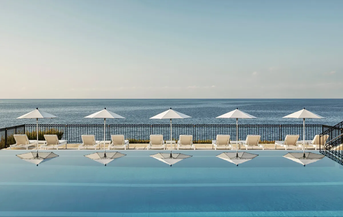 Outdoor pool with beach cabanas lined along calm Mediterranean waters