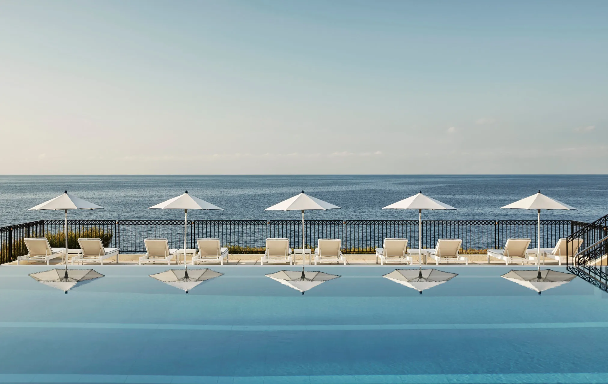 Outdoor pool with beach cabanas lined along calm Mediterranean waters