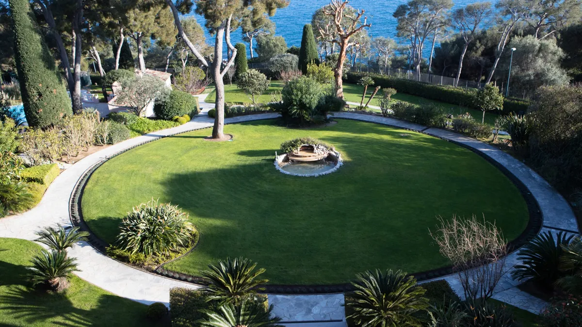 Circular lawn with central fire pit, trees, and sea view beyond