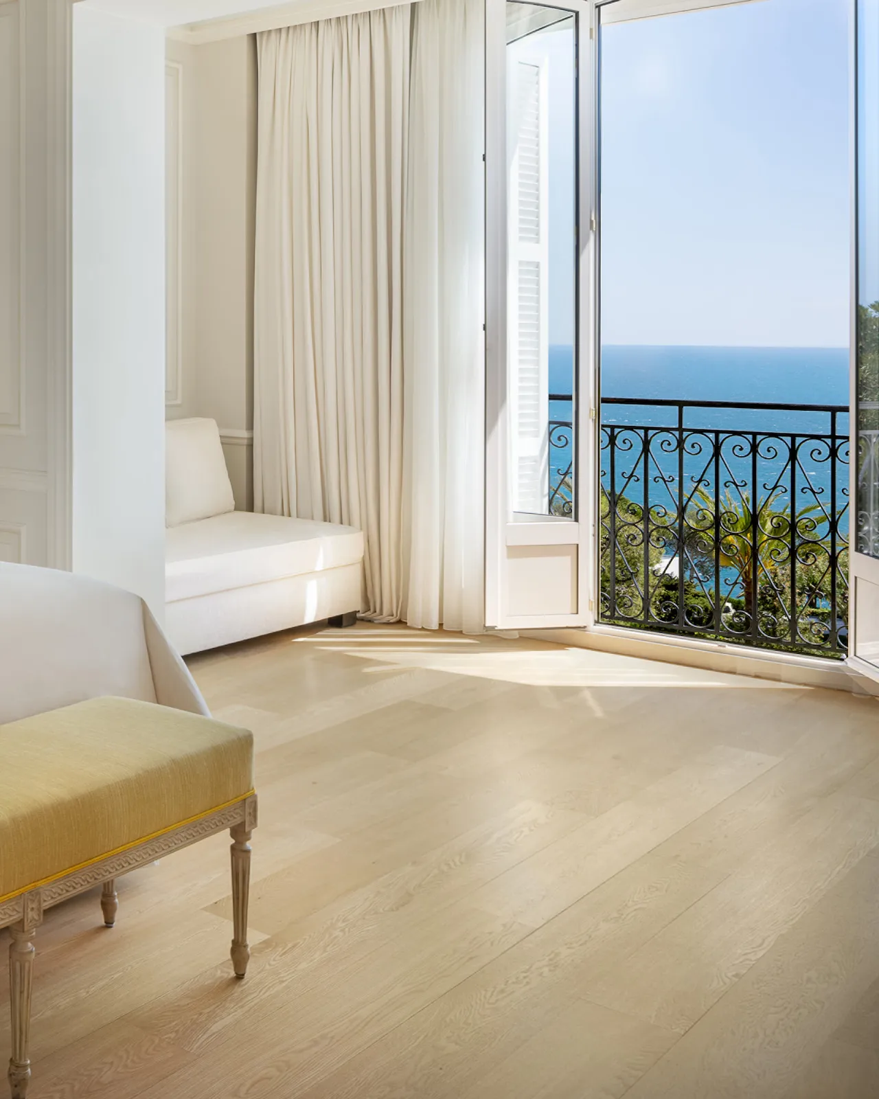 Light-filled suite with open balcony doors framing sea and coastline views