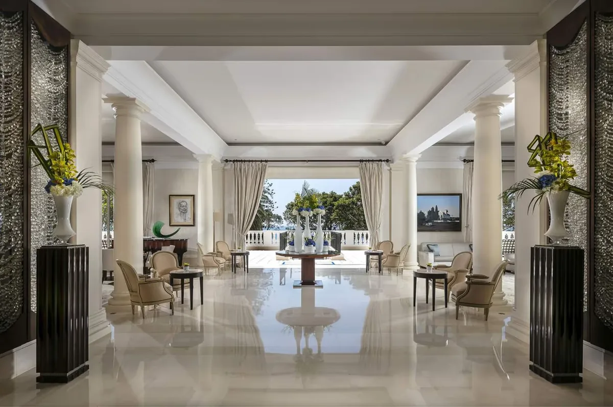 A grand hall with columns, polished floors, and sea views through open doors