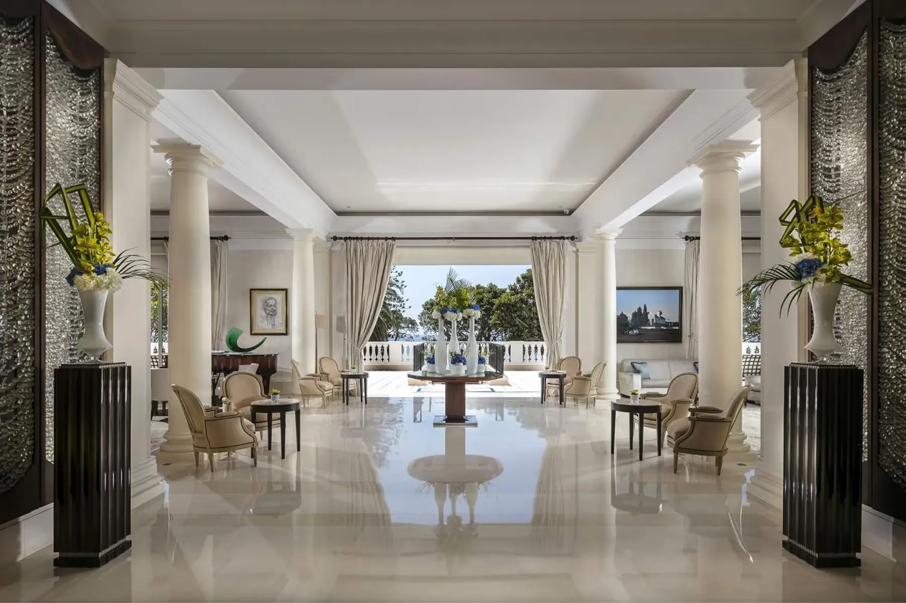 A grand hall with columns, polished floors, and sea views through open doors