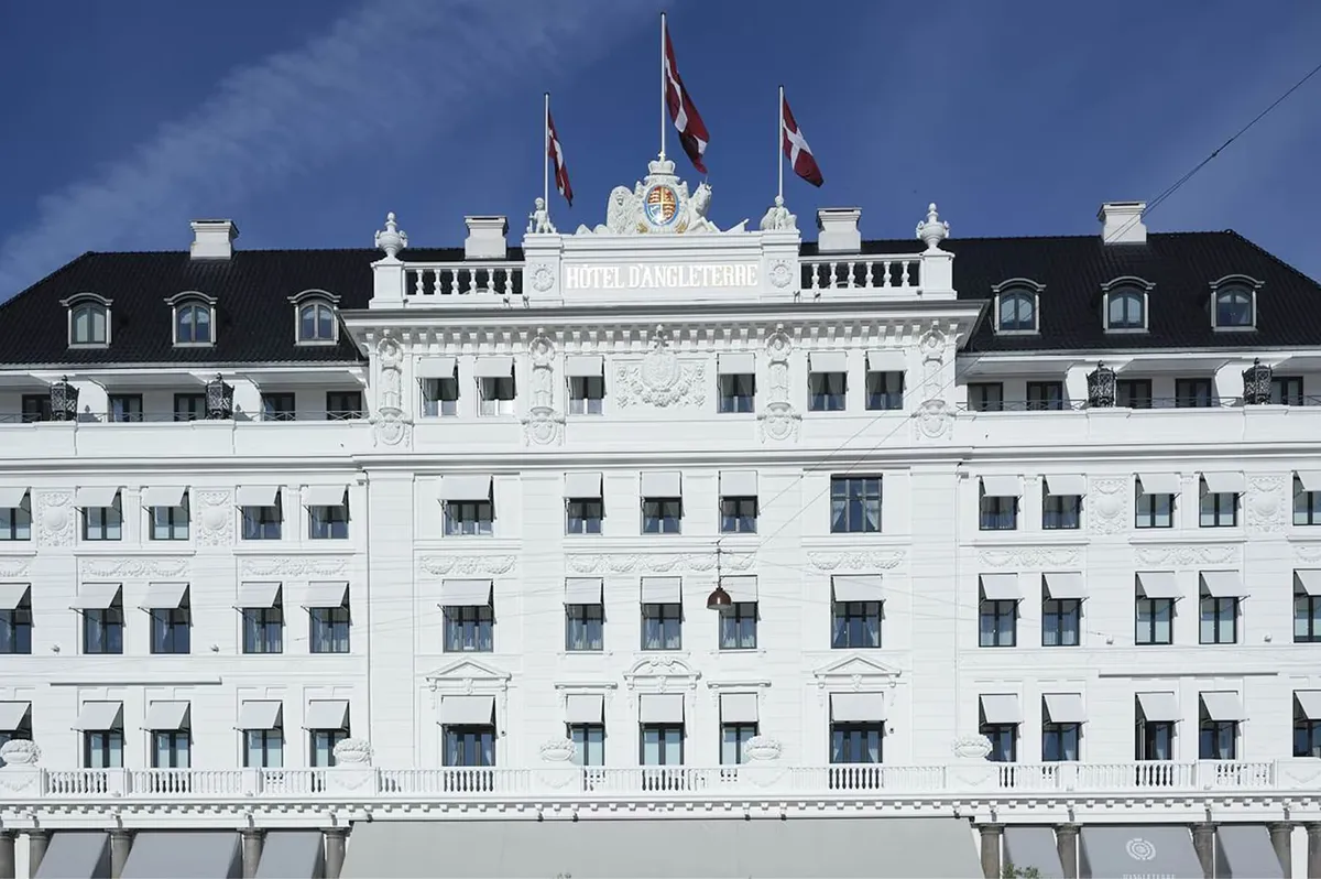 Pale facade with mansard roof and royal flags at Kongens Nytorv