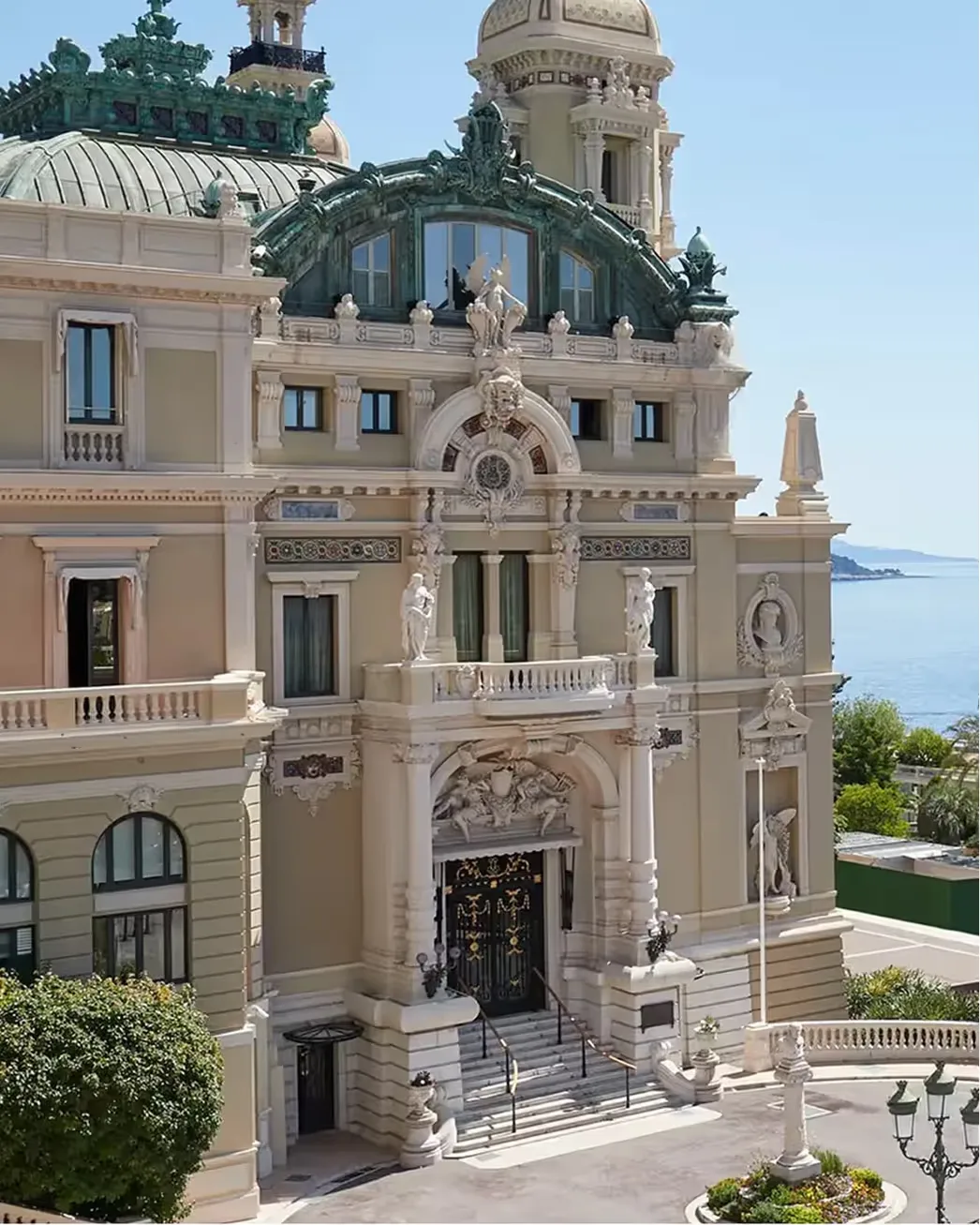 Facade in cream stone with arched entryway, sculptural details, and sea views behind