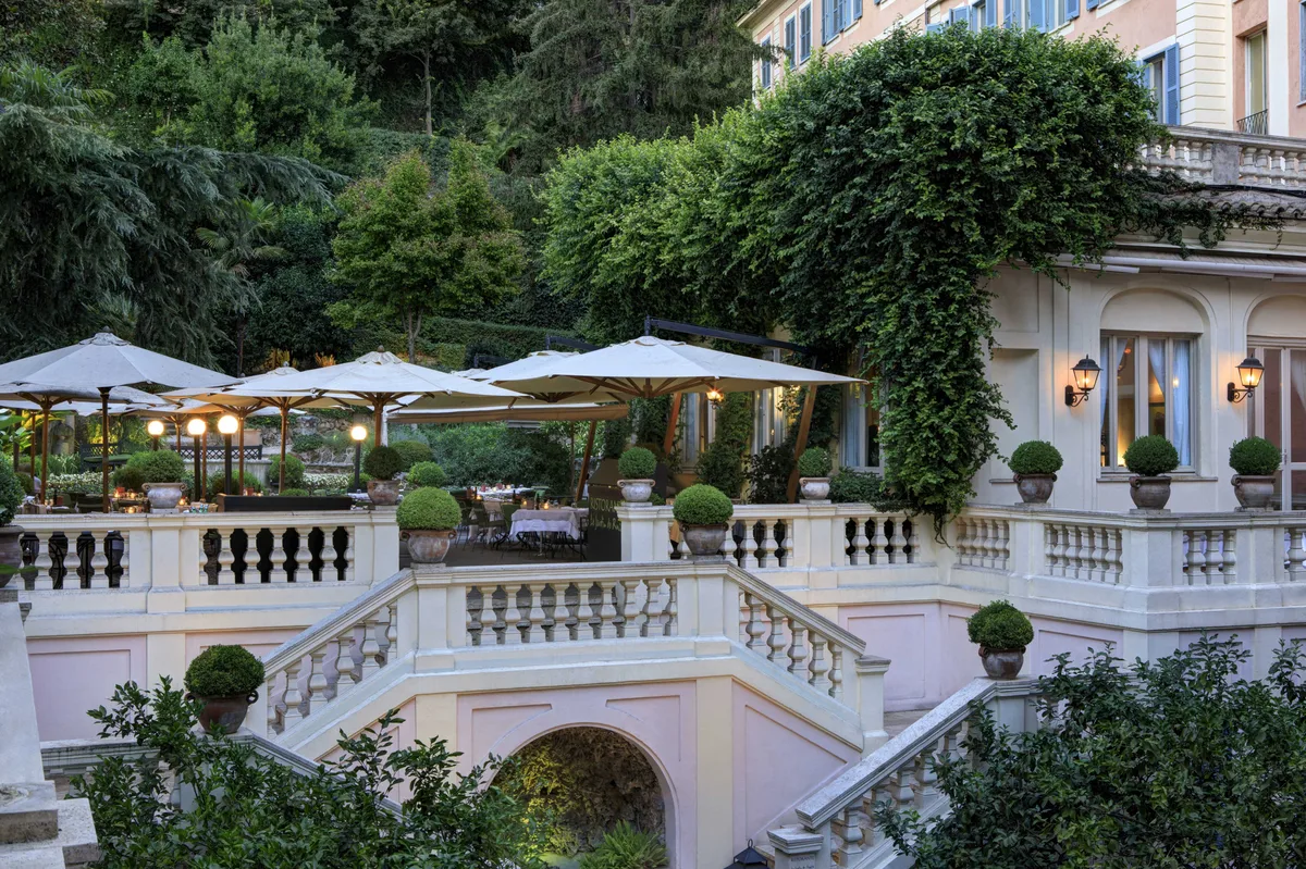 Tiered garden terrace with beige umbrellas, balustrade, and lush greenery