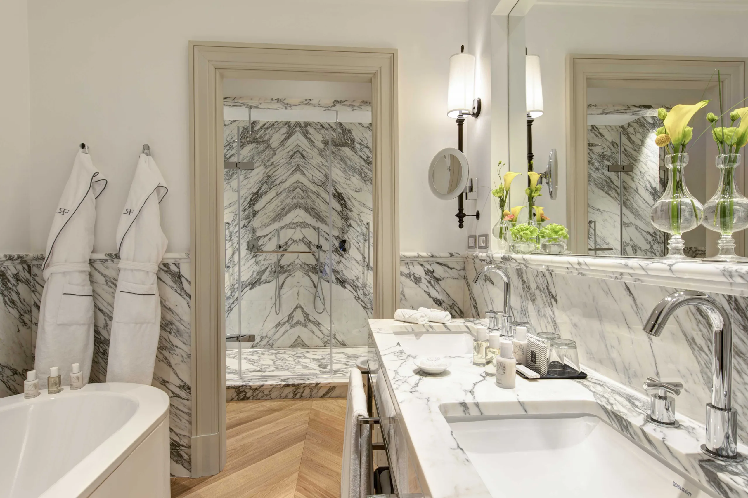 Marble bathroom with dual sinks, decorative panels, and white fixtures