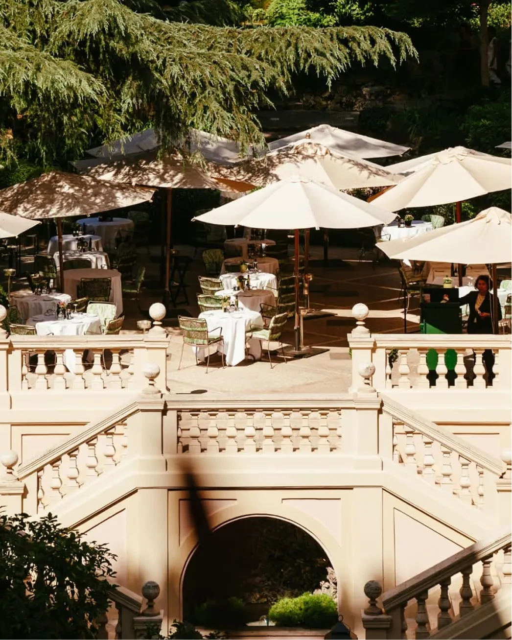 Dining terrace with green umbrellas and balustrade overlooking verdant gardens